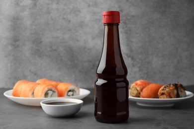 Photo of Tasty soy sauce and different types of sushi on grey table