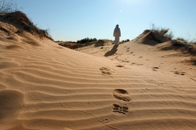 Photo of Man walking through desert, focus on footprints in sand