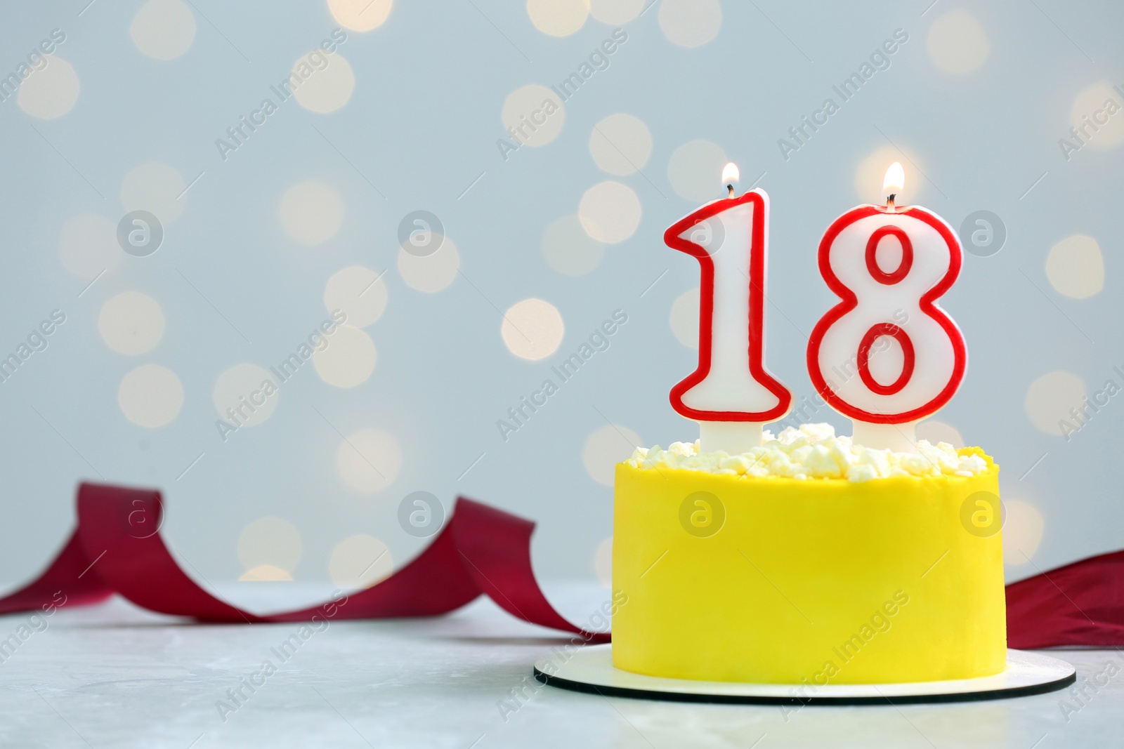 Photo of Coming of age party - 18th birthday. Delicious cake with number shaped candles on white table against blurred lights, space for text