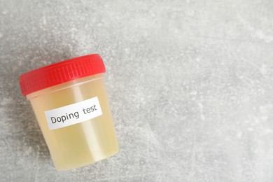 Photo of Jar of urine with words Doping test on light grey stone table, top view. Space for text