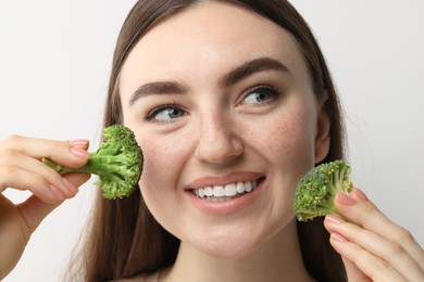 Photo of Smiling woman making fake freckles with broccoli and cosmetic product on light background, closeup