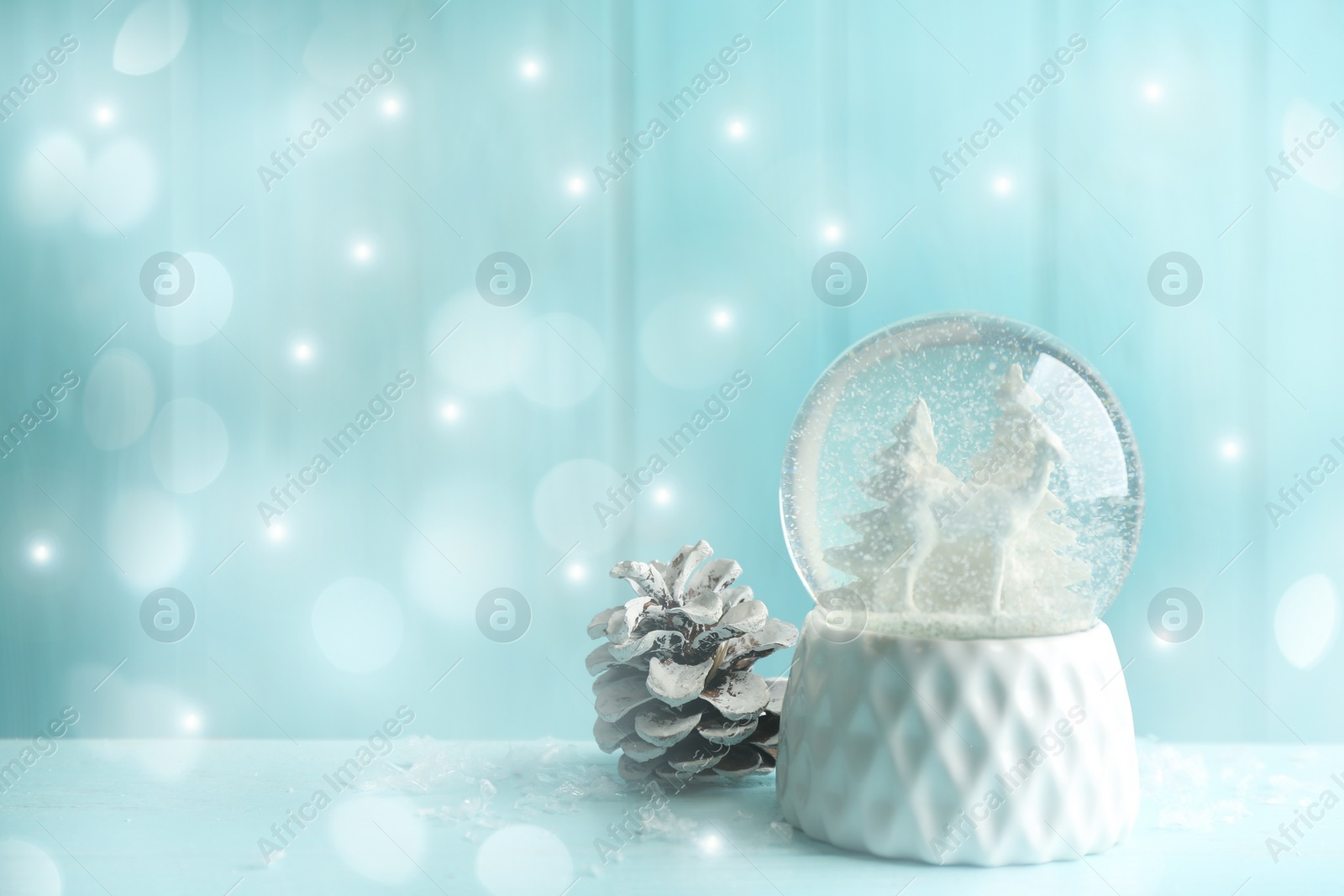 Image of Beautiful Christmas snow globe and fir cone on light blue background, bokeh effect. Space for text