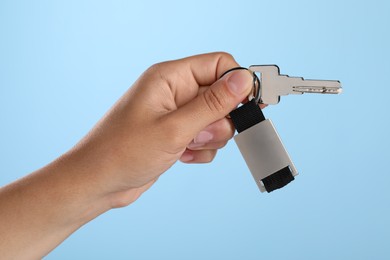 Photo of Woman holding key with keychain on light blue background, closeup