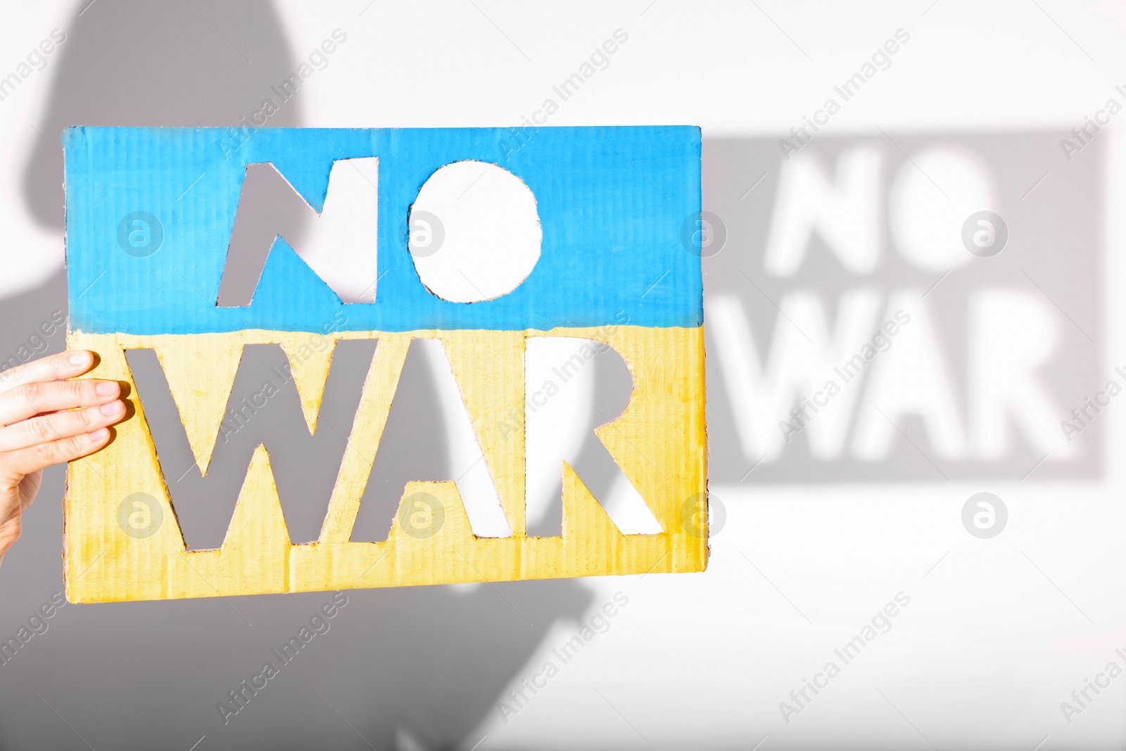 Photo of Woman holding poster in colors of Ukrainian flag with words No War on light background, closeup