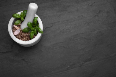Photo of Mortar with peppercorns, basil and garlic on black table, above view. Space for text