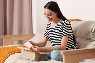 Photo of Happy young woman opening parcel on sofa at home. Internet shopping