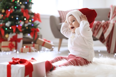 Cute baby in Santa hat on floor at home. Christmas celebration