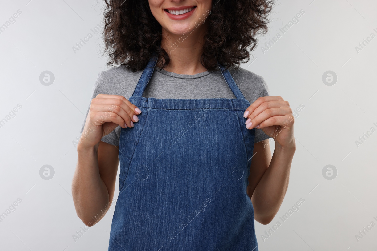 Photo of Woman wearing kitchen apron on light grey background, closeup. Mockup for design