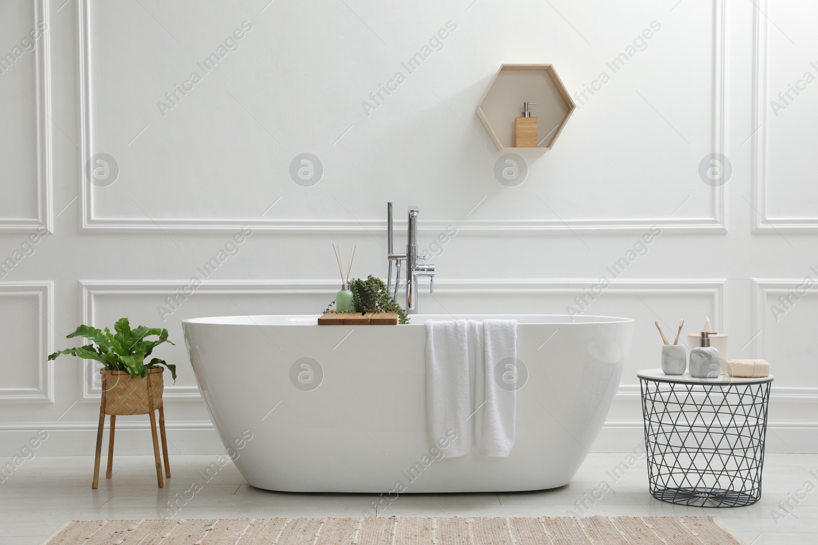 Photo of Modern ceramic bathtub and green plants near white wall in room