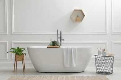 Modern ceramic bathtub and green plants near white wall in room