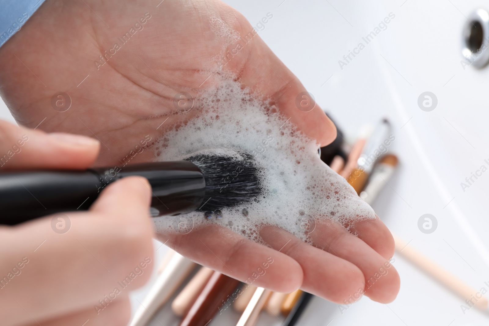 Photo of Woman washing makeup brush with soap, closeup