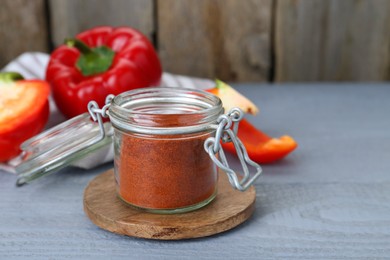 Photo of Jar with aromatic paprika powder and fresh bell peppers on grey wooden table