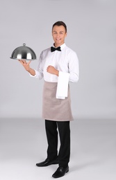 Photo of Waiter holding metal tray with lid on grey background