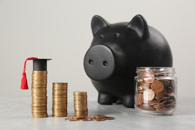 Scholarship concept. Piggy bank, graduation cap and coins on light grey table
