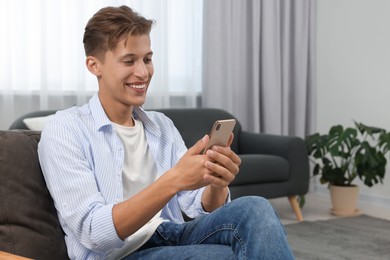Happy young man having video chat via smartphone on armchair indoors. Space for text