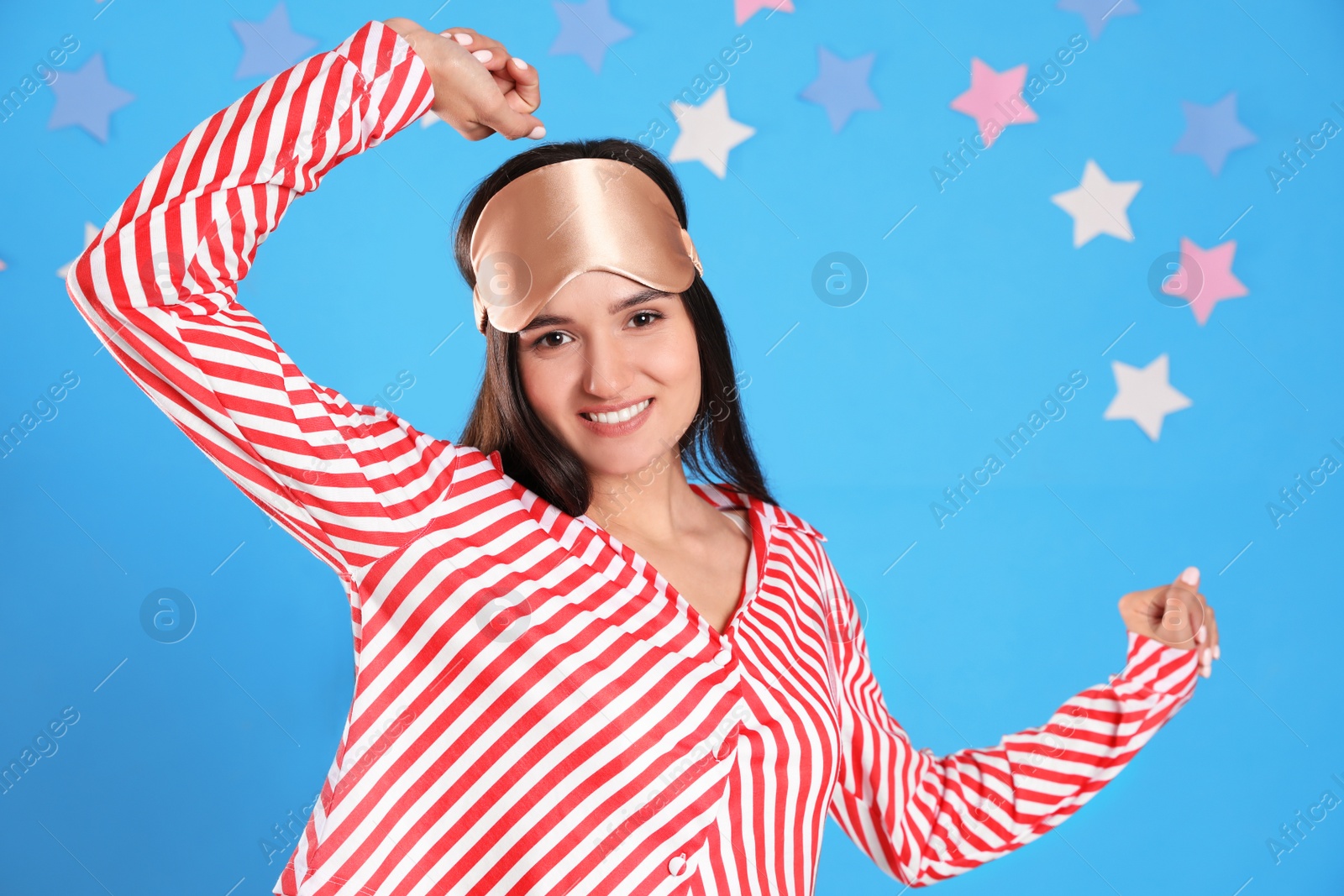 Photo of Beautiful woman wearing sleeping mask on light blue background. Bedtime