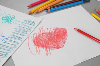 Photo of Cute children`s drawings and colorful pencils on grey table