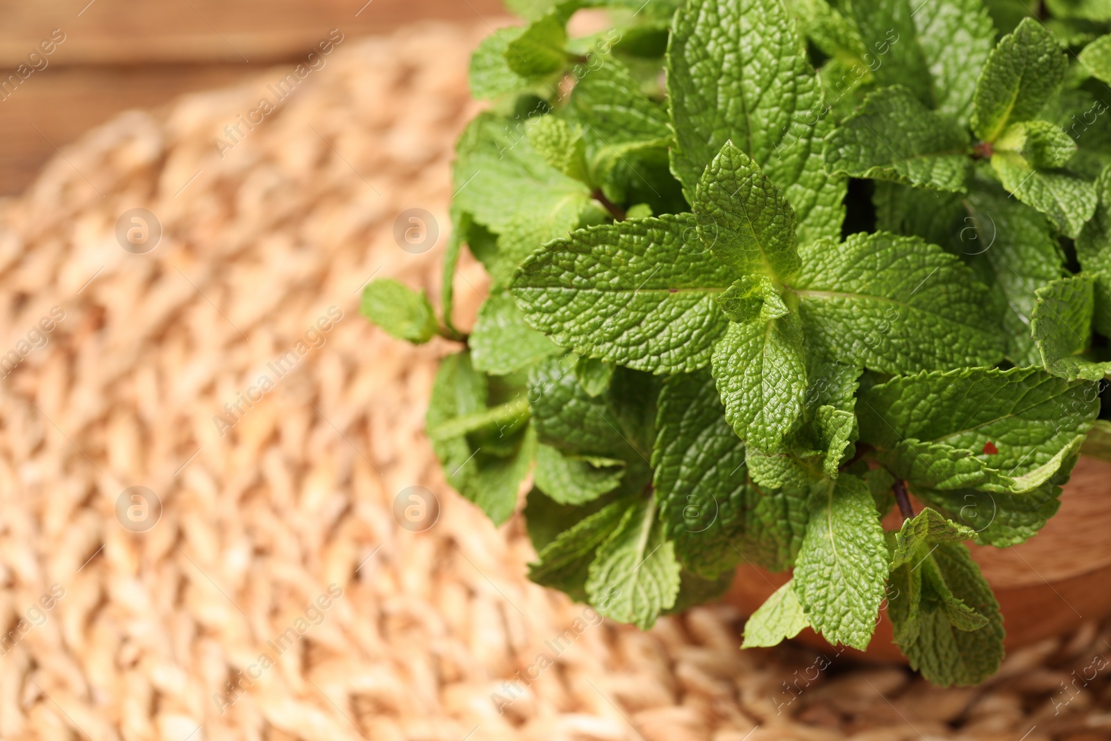 Photo of Bowl with fresh green mint leaves on wicker mat, closeup. Space for text