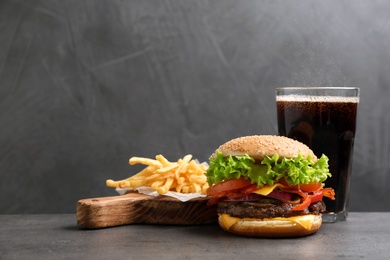 Photo of Burger with bacon, soda drink and french fries on table against grey background, space for text