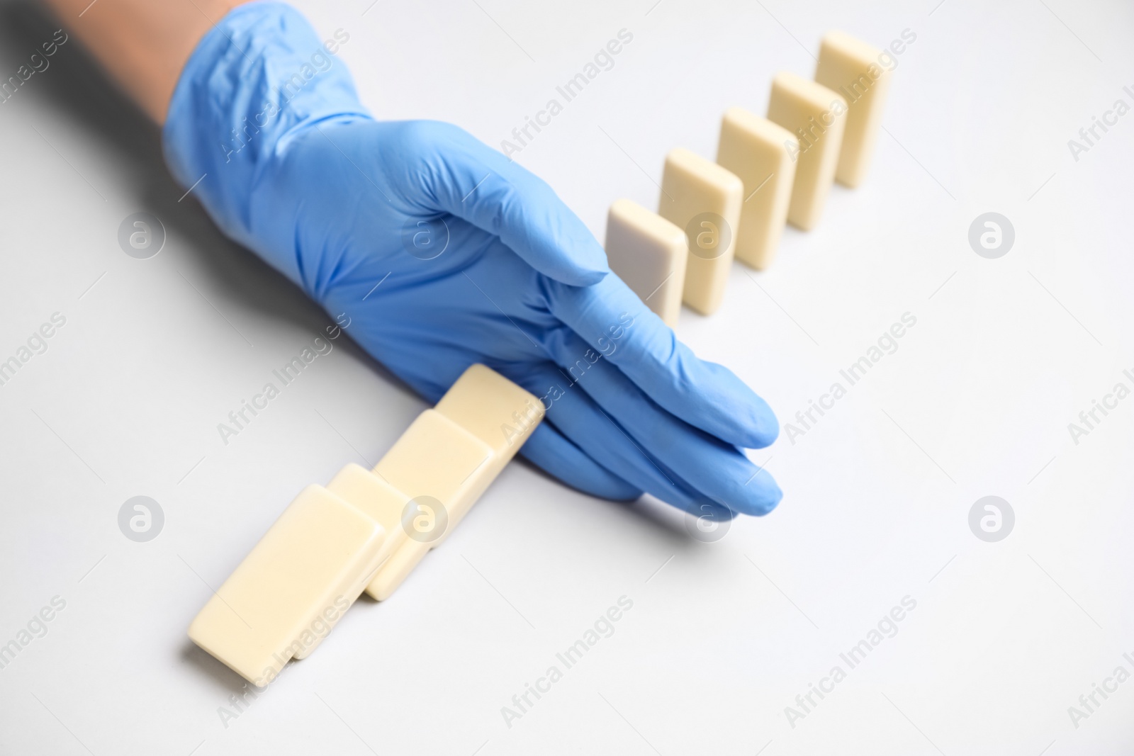 Photo of Doctor stopping domino effect on white background, closeup. Prevent spreading of coronavirus