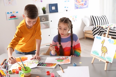 Photo of Little children painting picture at table indoors