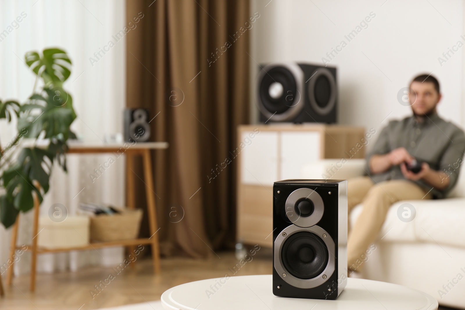 Photo of Man using remote to control modern audio speaker system in bright room