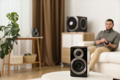 Photo of Man using remote to control modern audio speaker system in bright room