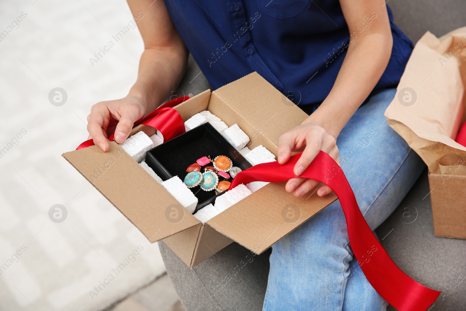 Photo of Young woman opening parcel on sofa in living room, closeup