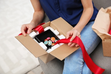 Young woman opening parcel on sofa in living room, closeup