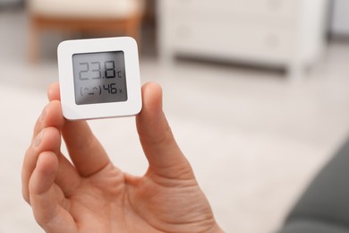 Photo of Woman holding digital hygrometer with thermometer at home, closeup. Space for text