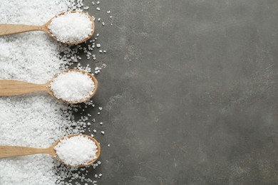 Photo of Natural sea salt and wooden spoons on grey table, flat lay. Space for text