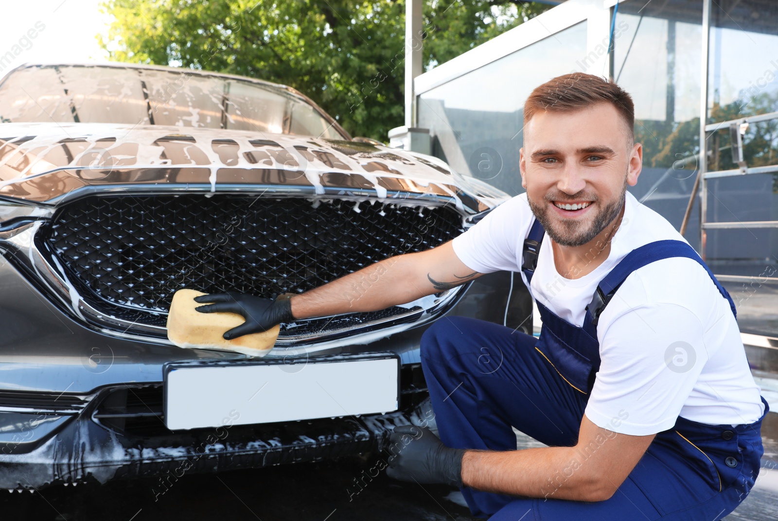 Photo of Young worker cleaning automobile with sponge at car wash