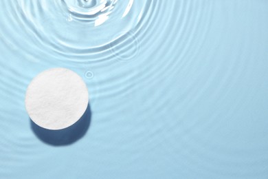Image of Cotton pad in micellar water on light blue background, top view. Space for text