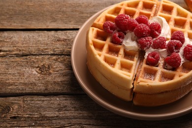 Photo of Tasty Belgian waffles with fresh raspberries and whipped cream on wooden table, space for text