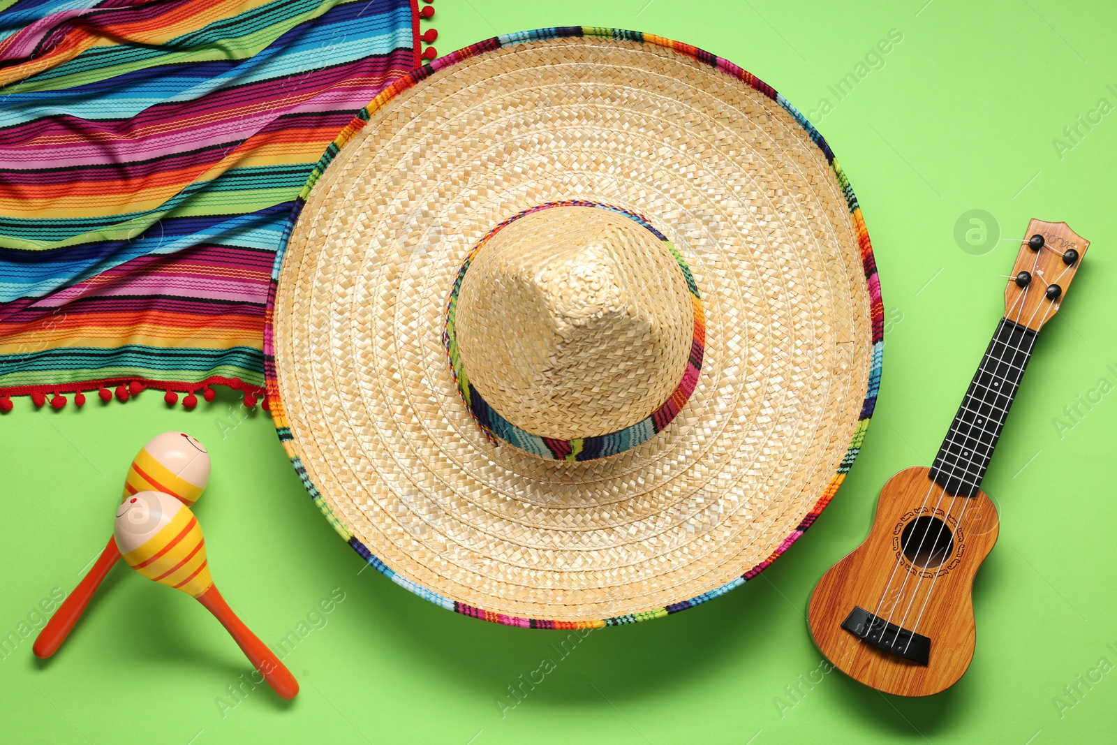 Photo of Mexican sombrero hat, guitar, maracas and colorful poncho on green background, flat lay