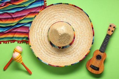 Mexican sombrero hat, guitar, maracas and colorful poncho on green background, flat lay
