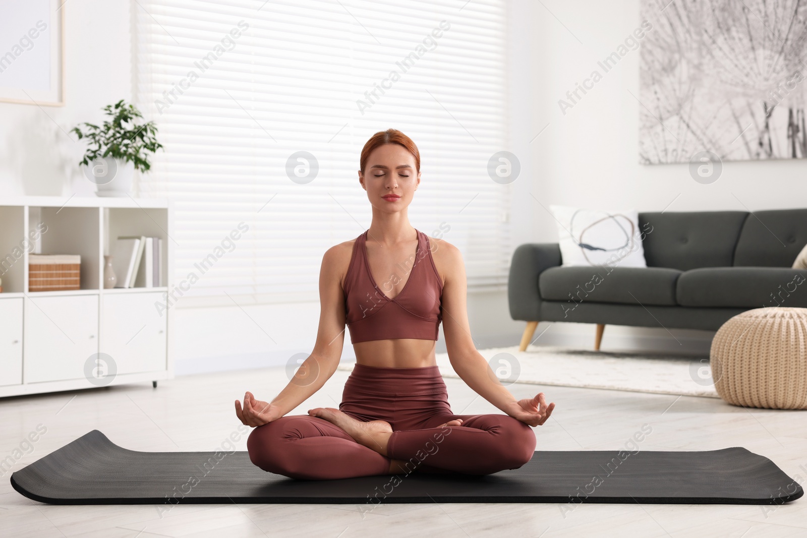 Photo of Beautiful young woman practicing Padmasana on yoga mat at home. Lotus pose