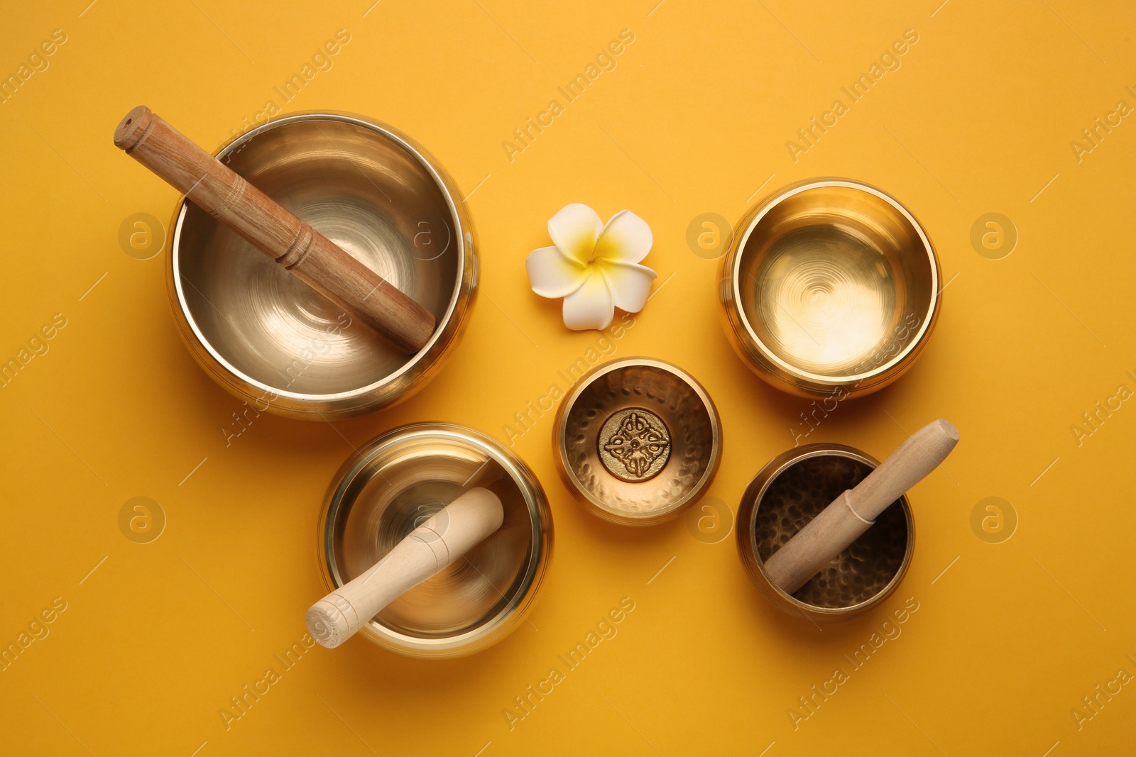 Photo of Golden singing bowls, mallets and flower on orange background, flat lay