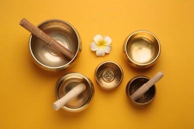 Photo of Golden singing bowls, mallets and flower on orange background, flat lay