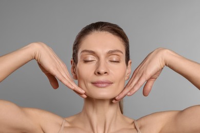 Photo of Woman massaging her face on grey background