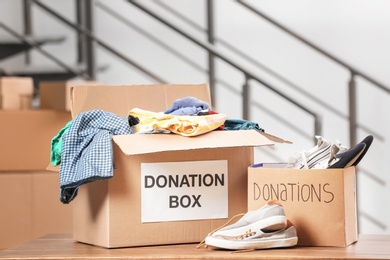 Photo of Donation boxes with clothes and shoes on table indoors