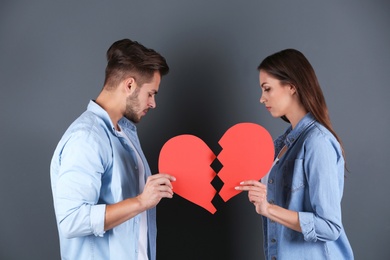 Young couple with torn paper heart on grey background. Relationship problems