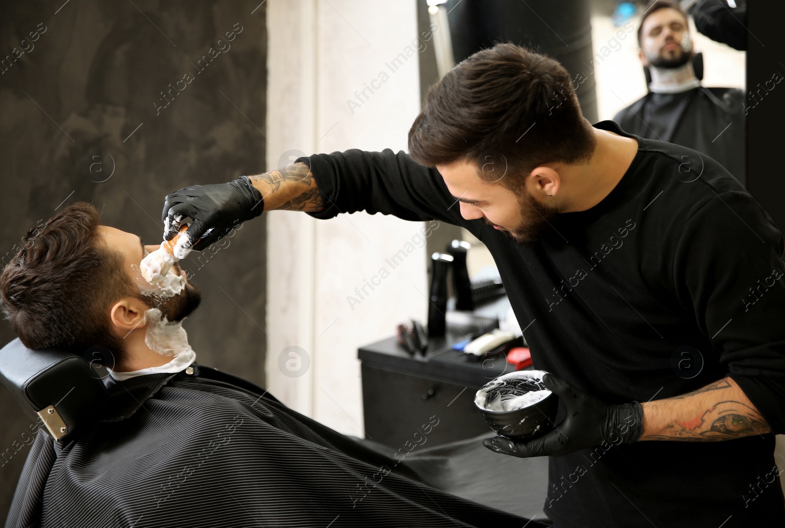 Photo of Professional hairdresser applying shaving foam onto client's skin in barbershop