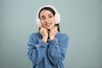 Photo of Beautiful young woman wearing earmuffs on light grey background