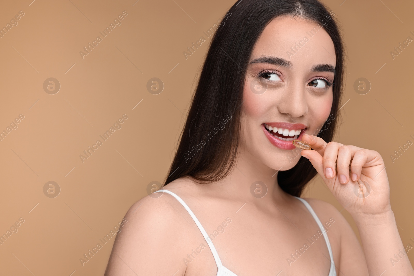 Photo of Beautiful young woman with vitamin pill on beige background. Space for text