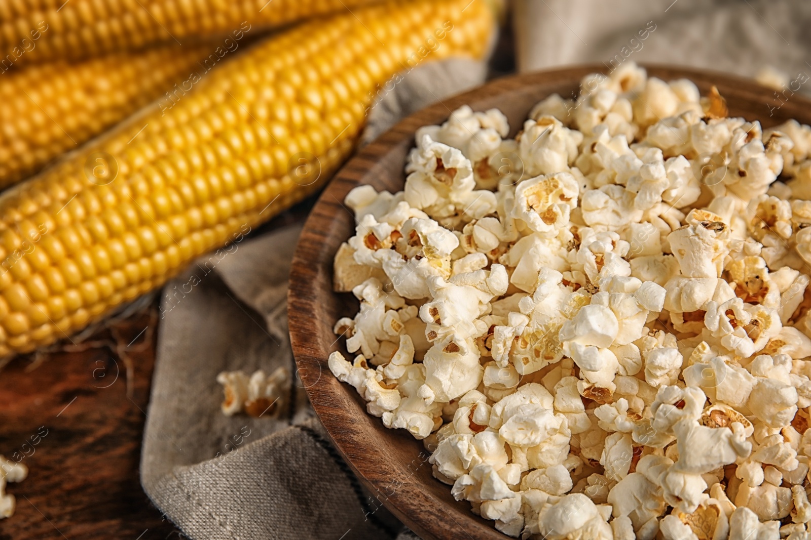 Photo of Bowl with delicious popcorn and cobs on table, closeup