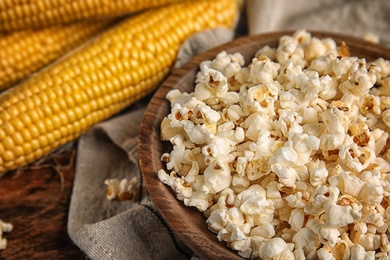 Bowl with delicious popcorn and cobs on table, closeup