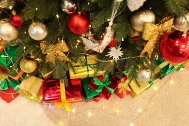 Photo of Decorated Christmas tree, beautiful gift boxes and festive lights on carpet, above view