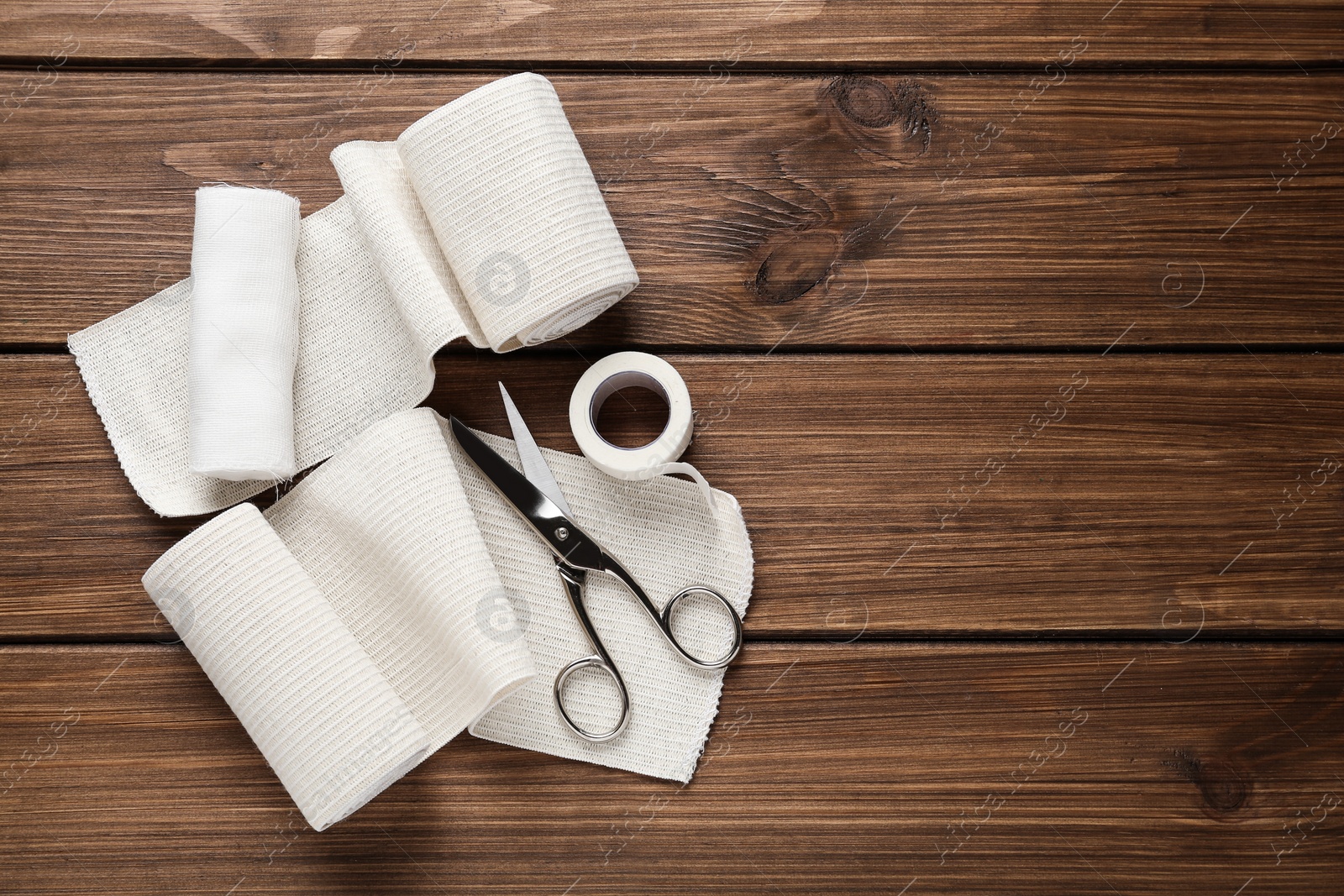 Photo of Medical bandage rolls, sticking plaster and scissors on wooden table, flat lay. Space for text