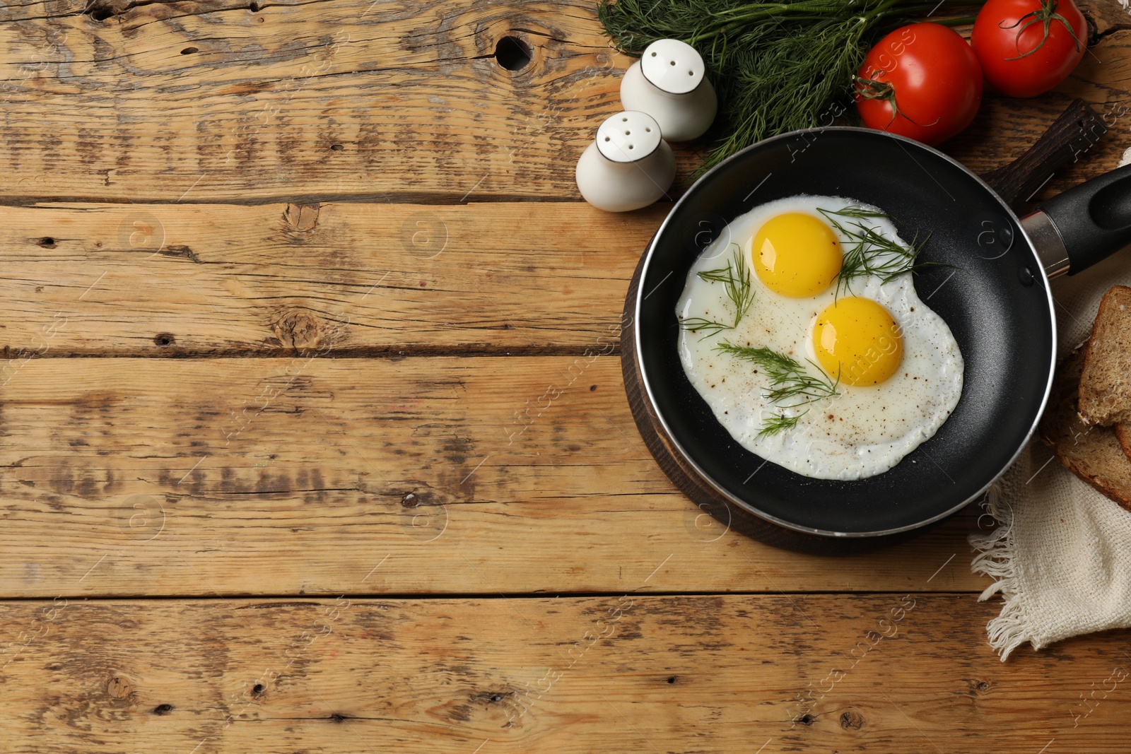 Photo of Frying pan with tasty cooked eggs, dill and other products on wooden table, flat lay. Space for text